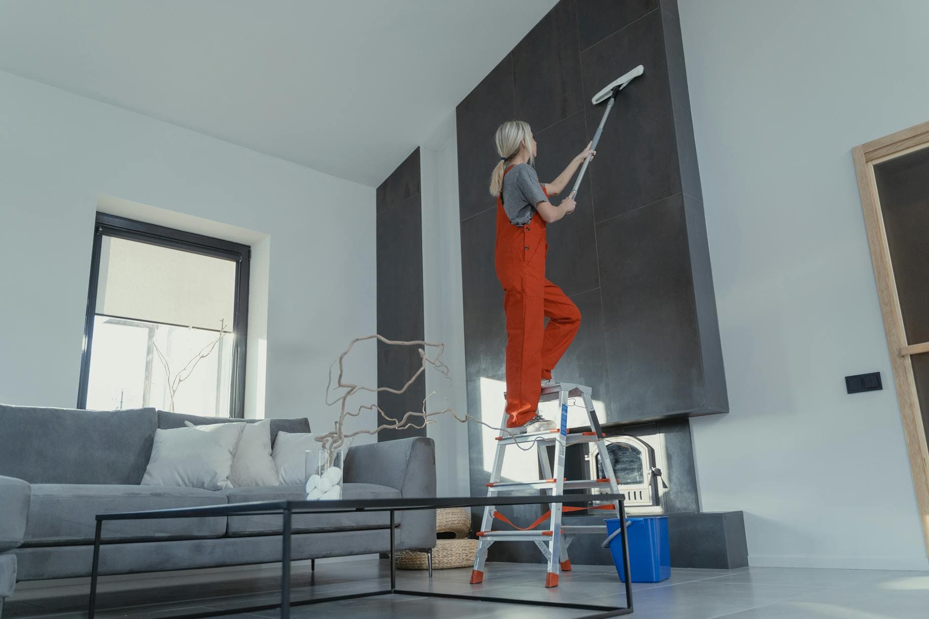 Your Business cleaner in red overalls on a ladder cleaning a high wall in a Manhattan apartment — Office Cleaning in Red Hook, Brooklyn