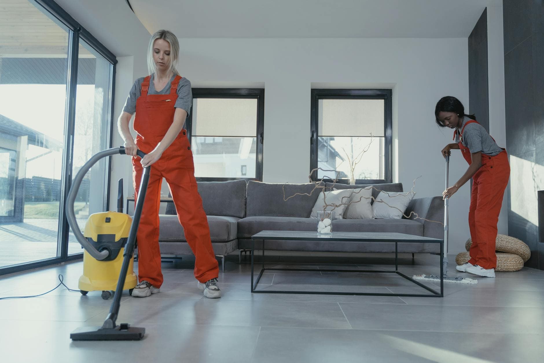 Two Your Business cleaners in red overalls vacuuming and sweeping a modern NYC living room — Office Cleaning in Chappaqua, Westchester