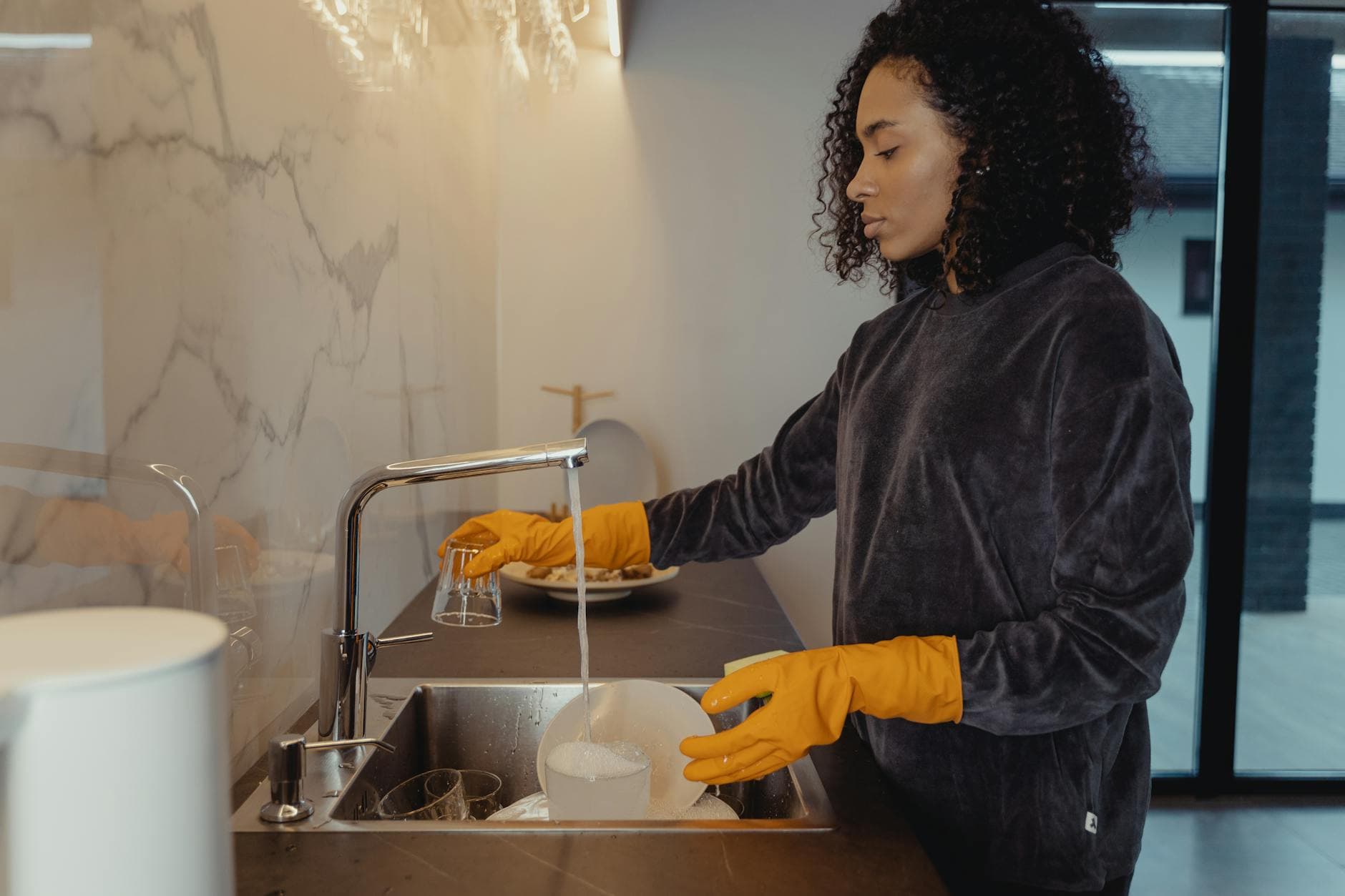 NYC maid wearing rubber gloves washing dishes in a modern Manhattan kitchen — cleaning services in Ditmars Steinway, Queens